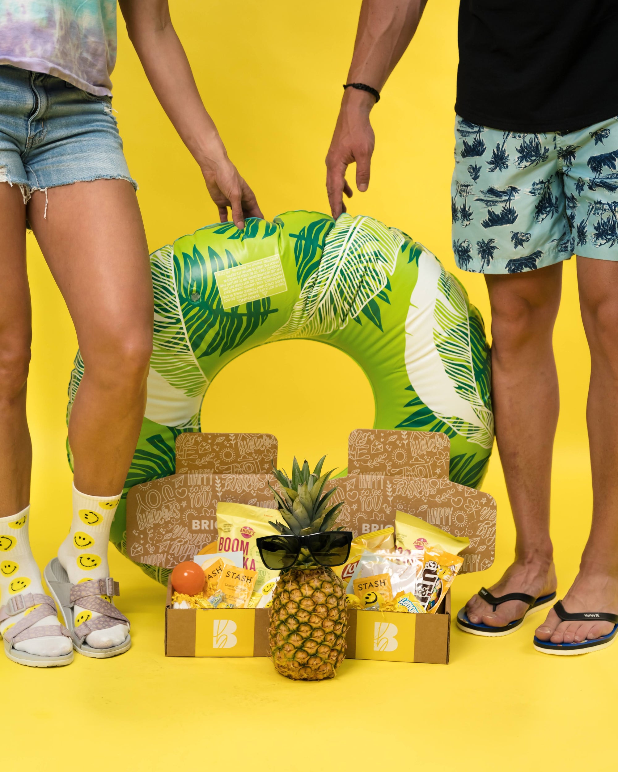Brightbox summer fun, with an inner-tube, pineapple with shades on, and the Sunshine Collection of curated boxes. Yellow backdrop 